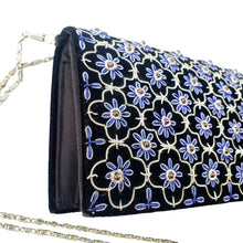 Load image into Gallery viewer, Side view of luxury black velvet evening clutch bag embroidered with silver quatrefoil cloverleaf pattern and blue flowers and embellished with genuine garnet gemstones, floral wedding clutch, silver and black and blue zardozi purse.