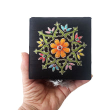 Load image into Gallery viewer, Close up view of embroidered orange floral medallion on black keepsake box with central ruby gemstone.