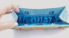 Load image into Gallery viewer, Turquoise blue clutch embroidered with multicolor flowers and embellished by star rubies, zardozi purse, interior view with full length gathered pockets. 
