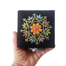 Load image into Gallery viewer, Close up view of embroidered orange floral medallion on black keepsake box with central ruby gemstone. 
