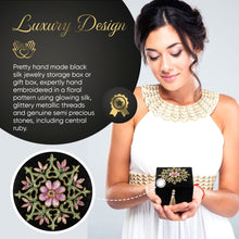 Load image into Gallery viewer, Model holding small black keepsake box embroidered with pink flower and inlaid with ruby gemstone. 
