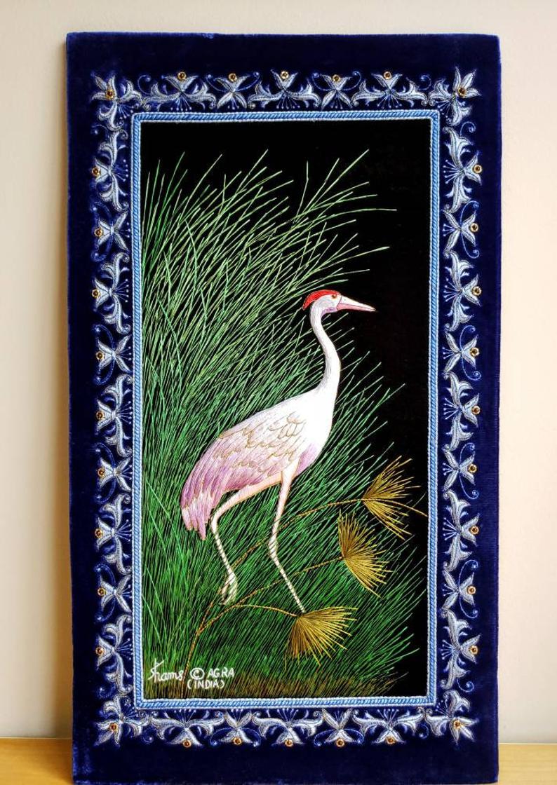 Embroidered silk bird tapestry, purple crane posing in grassland with ornate border, zardozi art. 