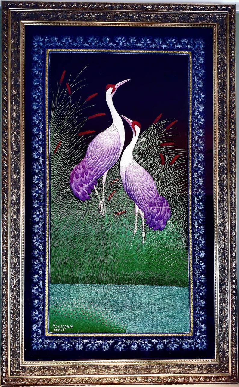 Embroidered bird wall art, two cranes with purple feathers standing in a grassy field embroidered on black velvet with an ornate border, framed, zardozi art. 
